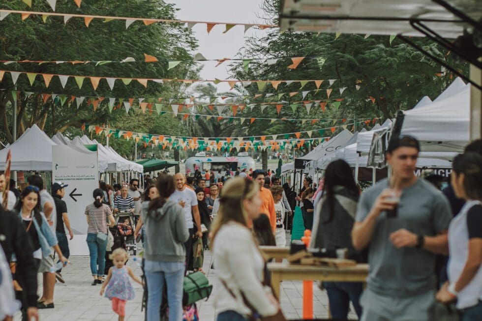 Large crowd of guests at a professionally staffed outdoor festival with vendor tents and colorful bunting decorations