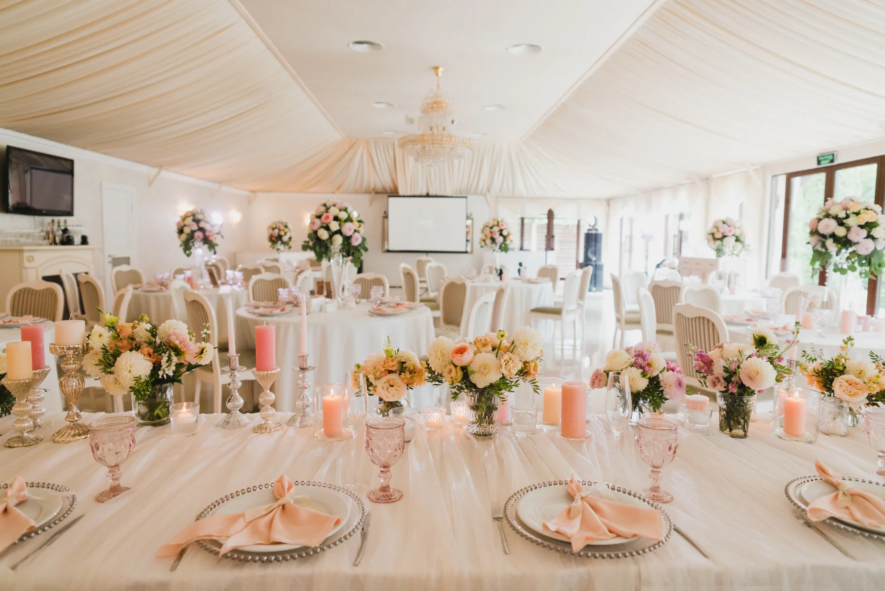 elegant-event-venue-floral-table-setting-hmg-plus. Elegant event venue set with floral centerpieces, candles, and place settings