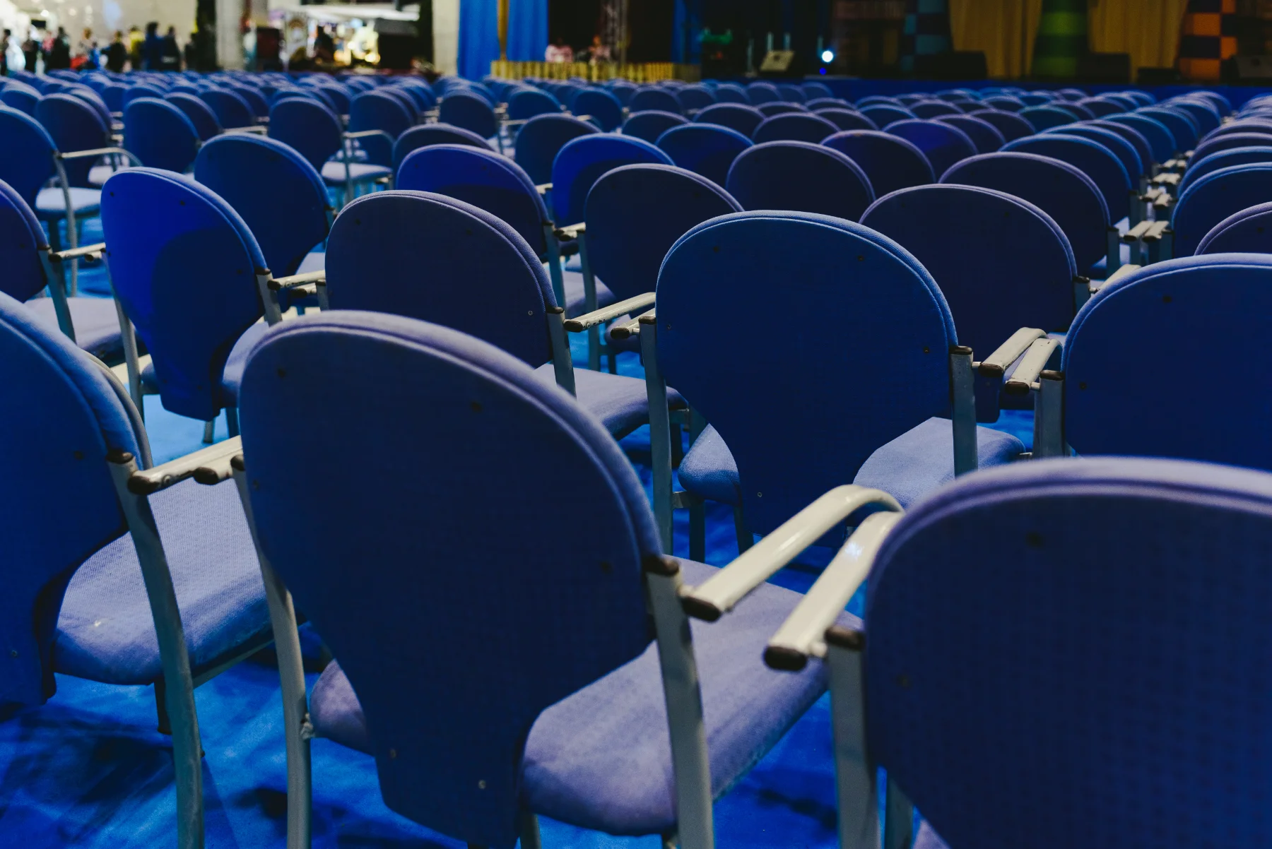 event-hall-blue-chairs-conference-seating-hmg-plus. Rows of empty blue chairs arranged in a conference or event hall